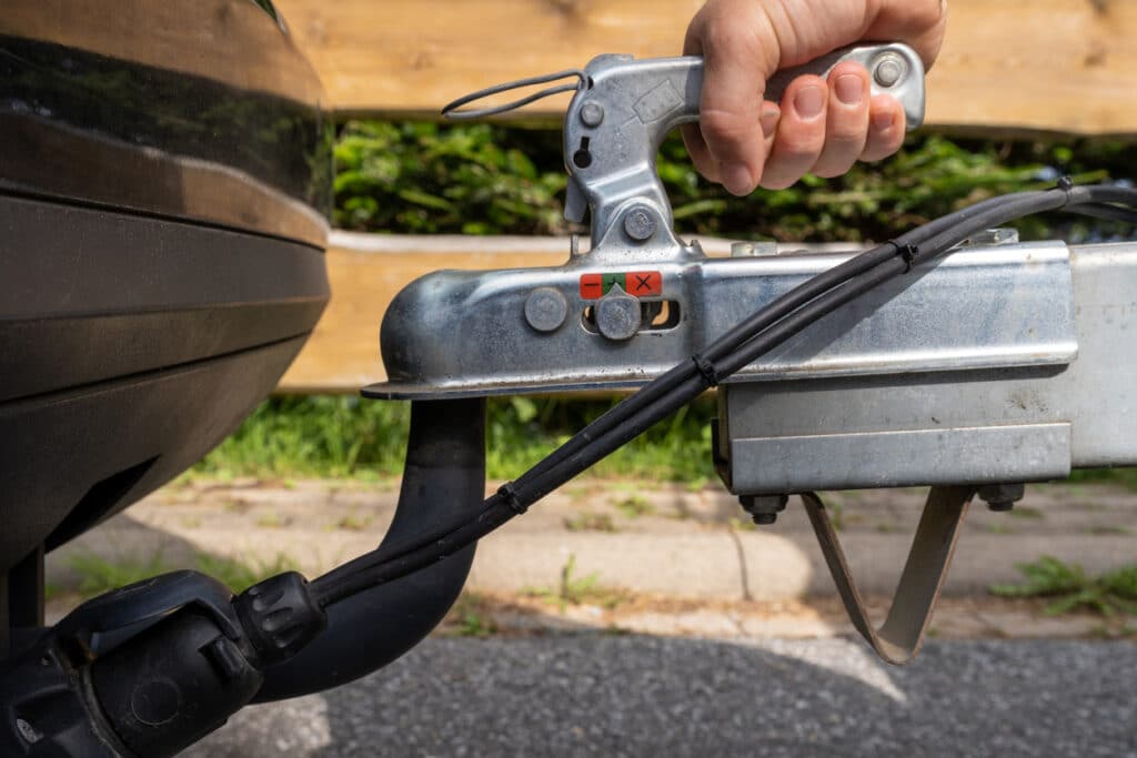 A hand checks the fixation of the trailer closed hitch lock handle on the towing ball